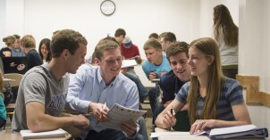 Three male students and one female student sit at desks and teach each other during a teaching session in an Essentials of Human Nutrition class.