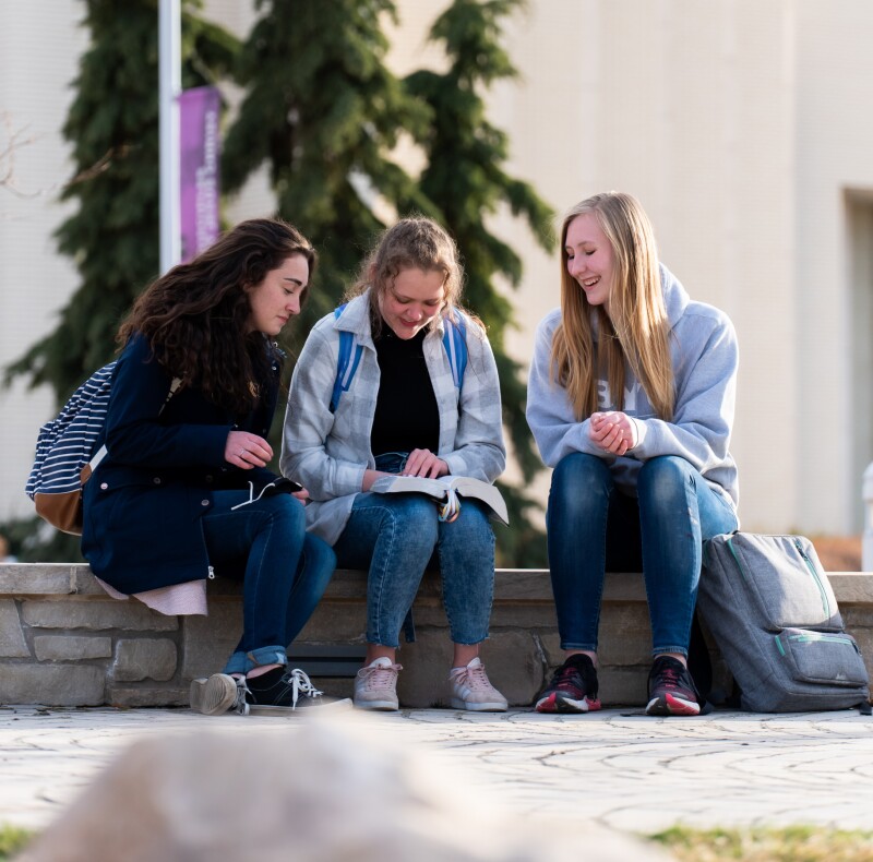 Three students reading scriptures in front of the Taylor building.