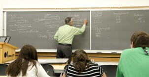 History Professor Bob Inama writes on a chalkboard while teaching his American Government class