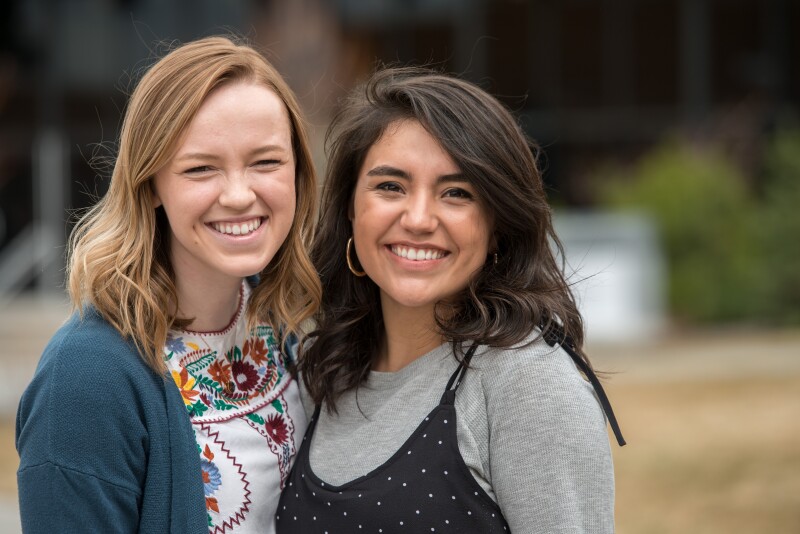 Two woman with their arm around one another, smiling at the camera