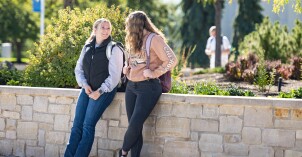 Two students leading on a wall, looking at eachother and smiling