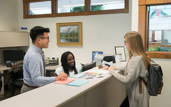 Two students help another at the Student Records office.