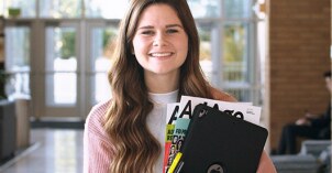 A Public Relations student holds her written work and smiles.