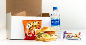 An I-Serve food delivery box featuring food contents: a sandwich, chips, bottle of water, and cookies.