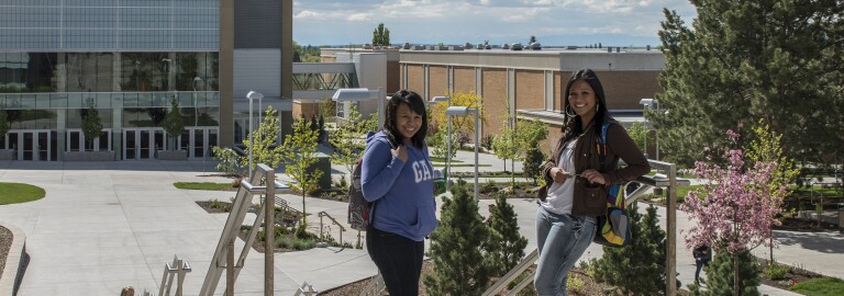 Two students on BYU-Idaho campus, outside the Manwaring center, smiling at the camera.