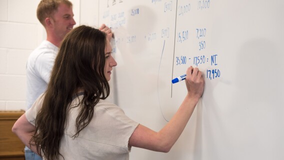 Accounting Students work to balance equations on a whiteboard.