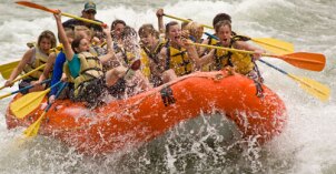 A group rafting down a river with a big splash of a wave comes over the front of the boat.