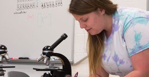 Biology student taking notes on a slide in a microscope