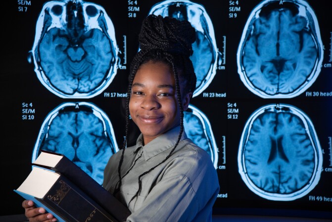 A Neuroscience student holds two thick books in front of brain x-rays.