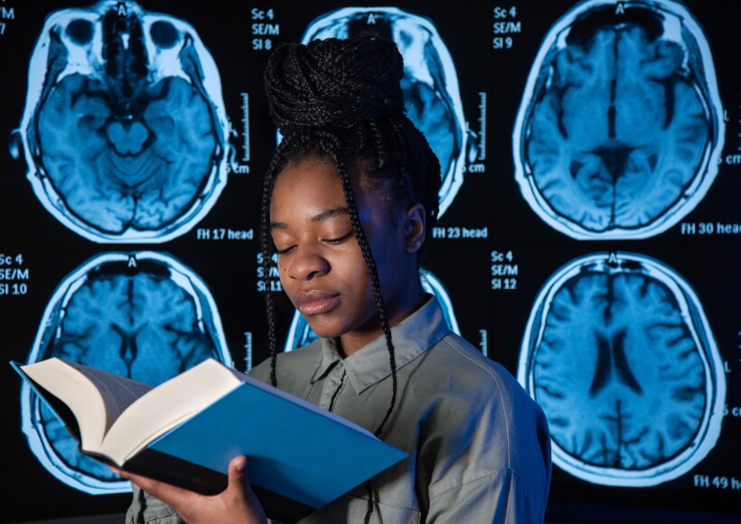 BYU-Idaho Psychology Student, Ayanna Manga, looking at a textbook with some brain scans in the background behind her.