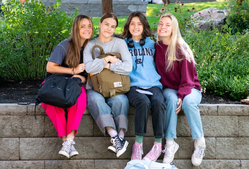 A group of BYU-Idaho girls sitting on a ledge, leaning together and smiling at the camera.