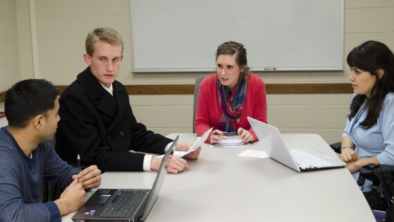 Four students sit at a table and discuss policy making processes in a public administrations class
