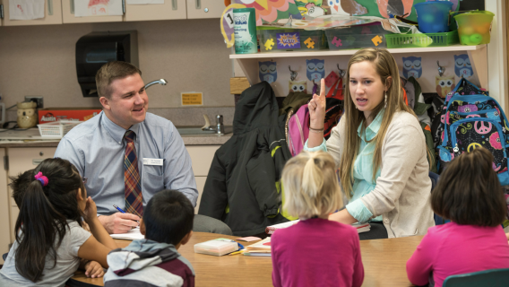 A student teacher engages with young children while a supervisor looks on