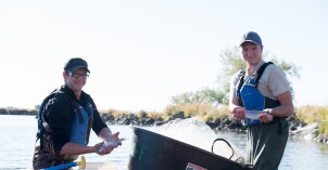 Two male students standing in a canoe holding fish on the Biology Fishing Field Trip.