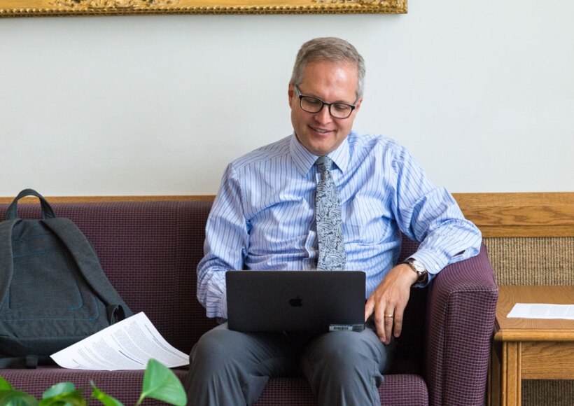 An employee sitting on a couch working on his laptop.