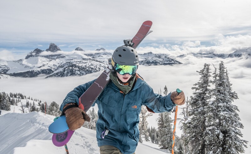 A skier with his skiis on his shoulder hiking up a mountain