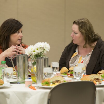 Two women, sitting at a table, eating lunch and talking to one another at the Women's Luncheon