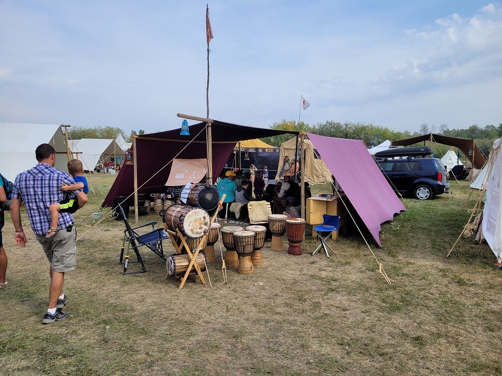 A man and a child walking towards a tent with drums outside.