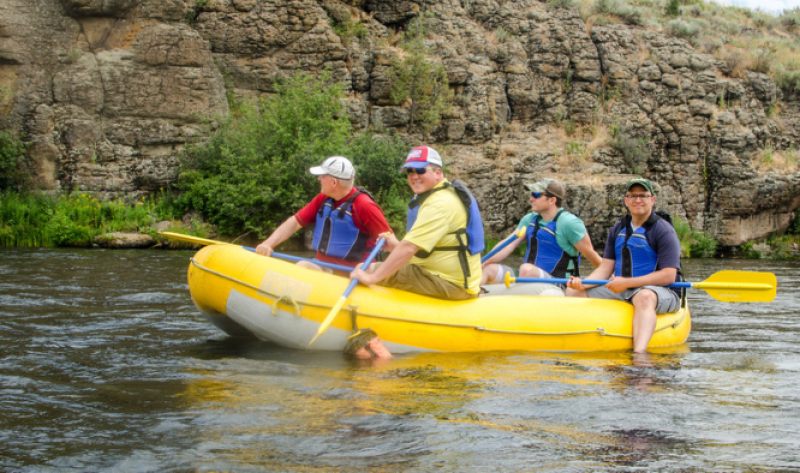 Four men in an outdoor river raft floating down a river.