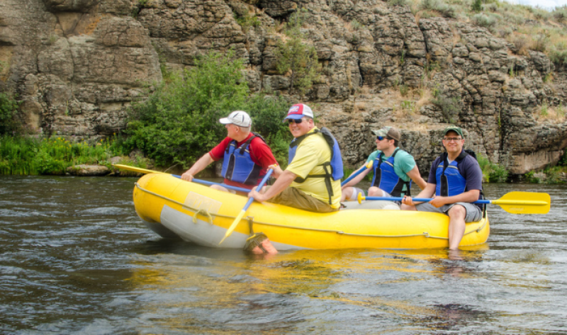 Four men in an outdoor river raft floating down a river. 