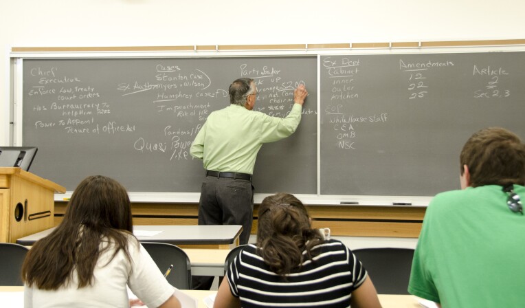 History Professor Bob Inama writes on a chalkboard while teaching his American Government class