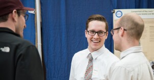 A male student smiles and listens as he interacts with an audience about his project at the Research and Creative Works Conference