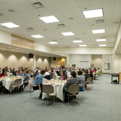 A big shot of all the women sitting at tables, listening to a speaker at the University Women's Association Luncheon.