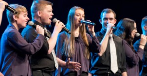 A group of students holding mics sing together on stage.