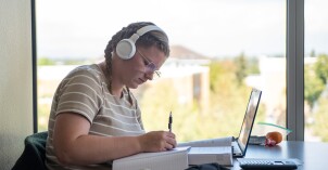 A girl wearing headphones, sitting at a table studying