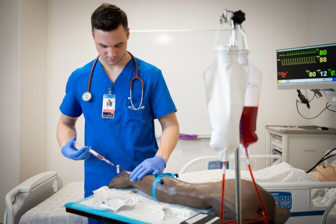 A nursing student practicing inserting an IV on a dummy arm.