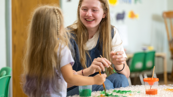 A child development student paints with a young girl.