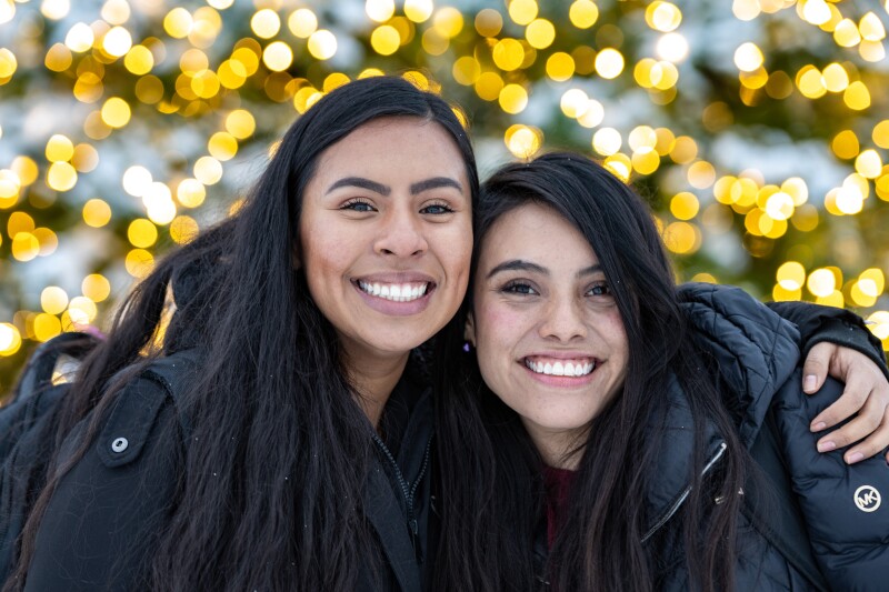 Two BYU-Idaho students pose for a picture, twinkling Christmas lights in the background.