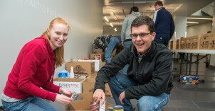 Two BYU-Idaho students smile while filling boxes with non-perishable food items during a stop and serve food drive project on the BYU-Idaho campus.