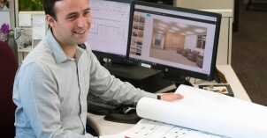A man sitting at a computer and looking at architectural plans.