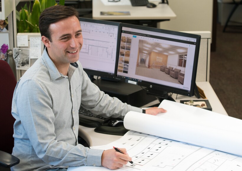 A man sitting at a computer and looking at architectural plans.