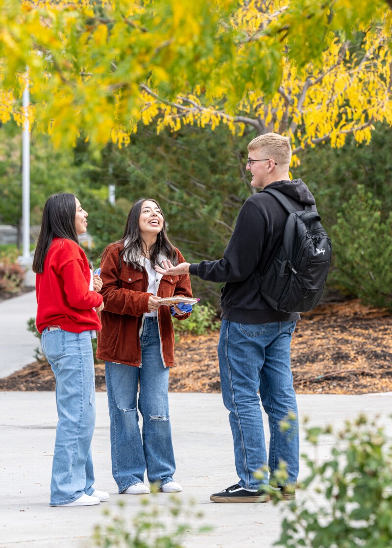 Two female students laugh with a male student near the Ricks Gardens on the BYU-Idaho campus.