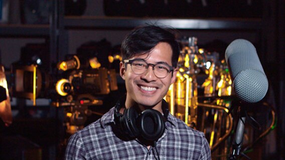 A Video Production student holds a mic and other equipment while smiling.